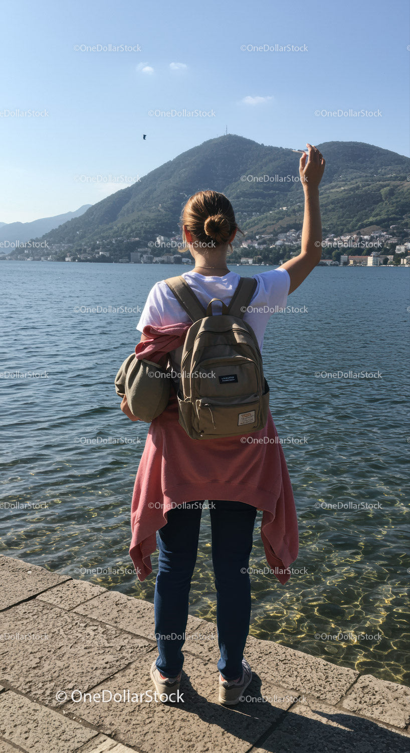 Young Woman with Backpack Taking Photo by Lake with Mountain View