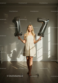 Young woman celebrating 17th birthday with balloons indoors