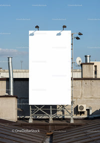 Blank vertical billboard on urban rooftop under blue sky