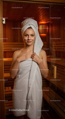 Young Woman Relaxing in Sauna with Towel Wrap in Wellness Center
