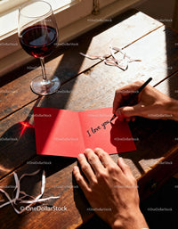 Handwriting a romantic love note beside red wine glass