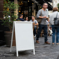 Blank sidewalk sign outside busy urban cafe