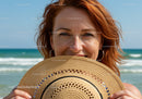 Joyful Red-Haired Woman Holding Straw Hat on Beach During Sunny Day