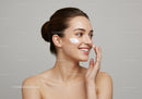 Young Woman Applying Facial Moisturizer with Bright Smile in Studio