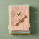 Stack of pastel baby blankets with wooden rattle and pacifier