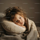 Thoughtful child resting on pillow wrapped in blanket