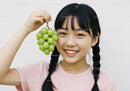 Smiling Girl Holding Green Grapes Among Her Black Braids