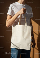 Casual man holding blank beige tote bag in warm light