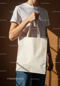 Casual man holding blank beige tote bag in warm light