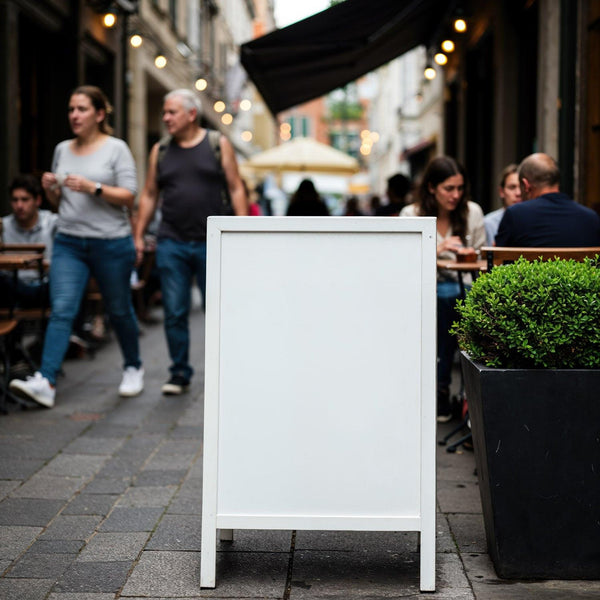 Blank white sidewalk sign in busy outdoor cafe alley JPG Mockup Image