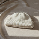 Cozy white knit beanie hat on beige fabric surface