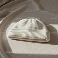 Cozy white knit beanie hat on beige fabric surface