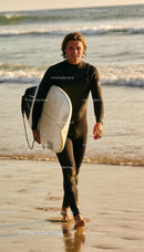 Surfer in wetsuit walking on beach at sunset