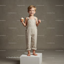 Smiling toddler holding cupcake in beige overalls