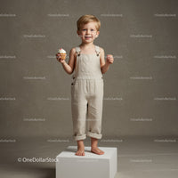 Smiling toddler holding cupcake in beige overalls