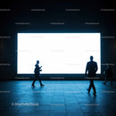 Silhouettes of business people walking by illuminated screen