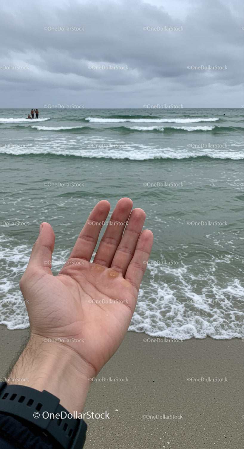 Otwarta dłoń z meduzą na plaży pod zachmurzonym niebem