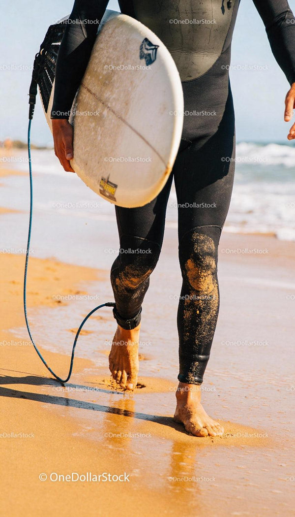 Surfer walking barefoot on sandy beach with board