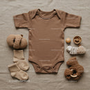 Neutral toned baby clothing and soft toys flat lay