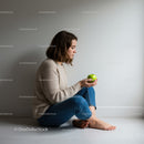 Young woman sitting on floor holding green apple thoughtfully