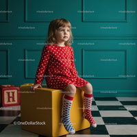 Little girl in red polka dot dress sitting on yellow cube