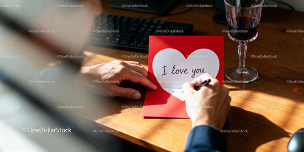 Man writing I love you message in red card at desk