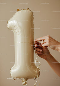 Hands tying ribbon on golden number one balloon