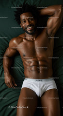 Smiling muscular man relaxing on dark green bed linens