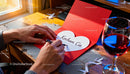 Handwritten love note on red card near wine glass