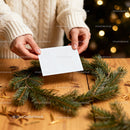 Hands Holding Blank Card Over Pine Wreath on Wooden Table JPG Mockup Image preview