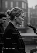 Elegant Woman in Black Blazer Speaking at City Street Microphone