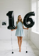 Teenage girl standing barefoot holding 16 balloons