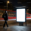 Man Walking Past Illuminated Bus Stop Advertisement at Night