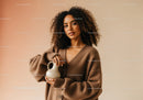 Elegant Woman in Brown Cardigan with Curly Hair Holding Vase