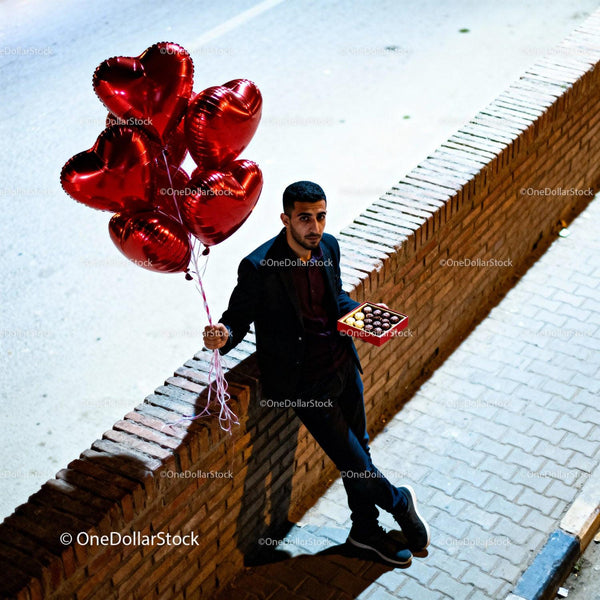 Man holding heart balloons and chocolates on street