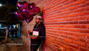 Man holding heart-shaped balloons and chocolates at night