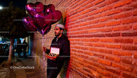 Man holding heart-shaped balloons and chocolates at night