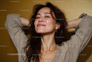 Confident Woman Smiling with Hands Behind Head in Warm Studio Setting