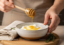 Close-up of Honey Dripping into Yogurt Bowl with Herbs and Wooden Spoon