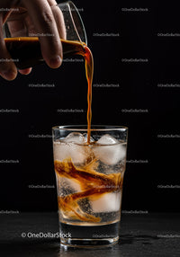 Pouring coffee over ice in a clear glass with soda