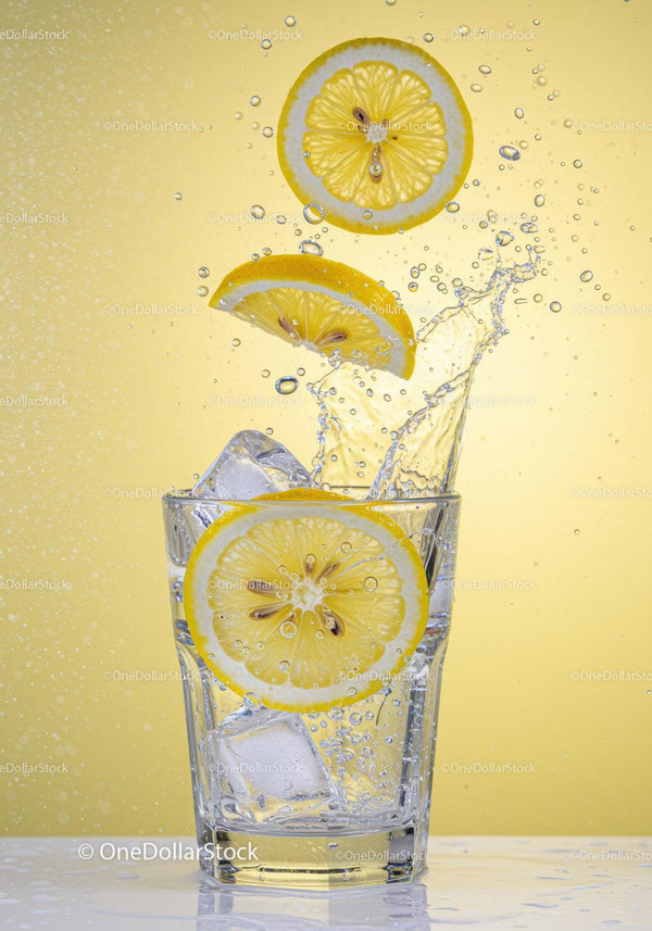Fresh lemon slices splashing into clear water glass