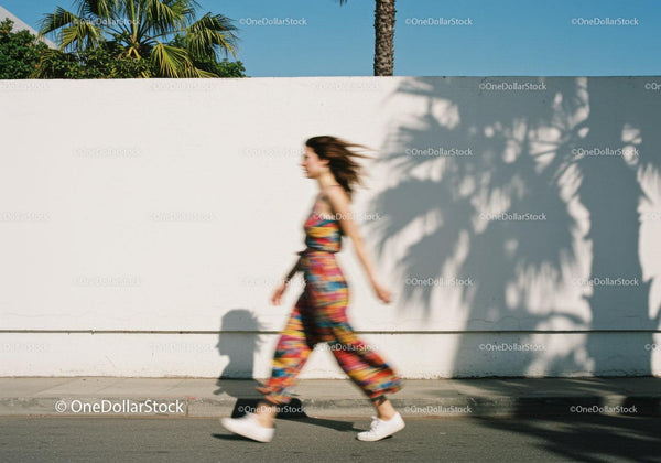 Woman walking past white wall with palm tree shadows JPG Mockup Image