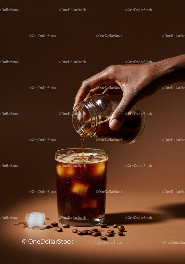 Hand pouring cold brew coffee into glass with ice cubes