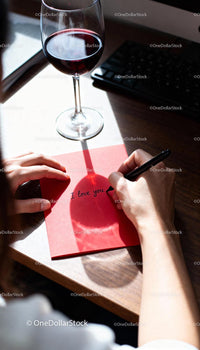 Writing a heartfelt love note beside red wine glass