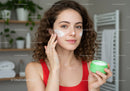 Young Woman in Red Applying Face Cream with Skincare Product in Bathroom