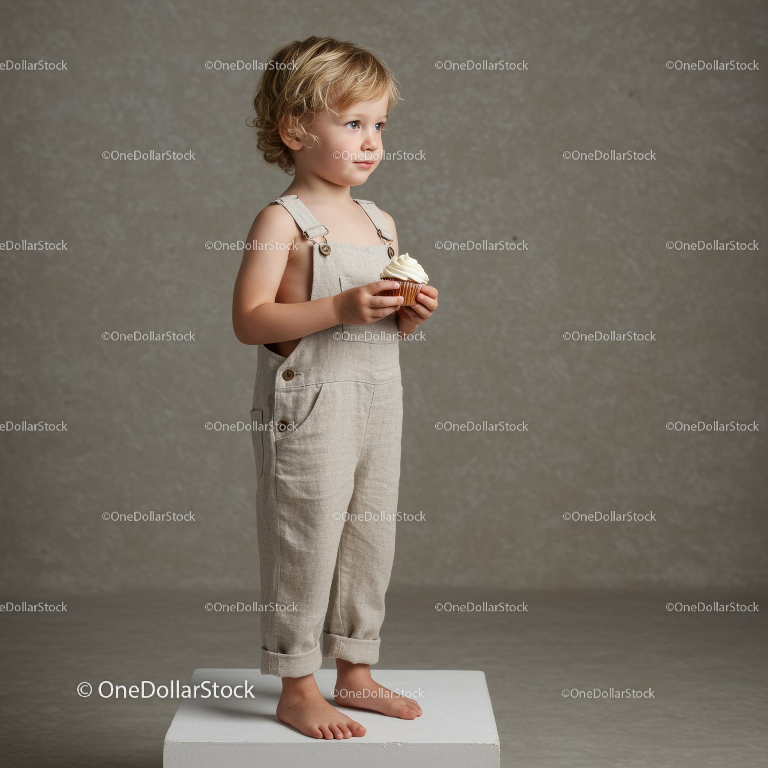 Toddler boy holding cupcake standing on white block