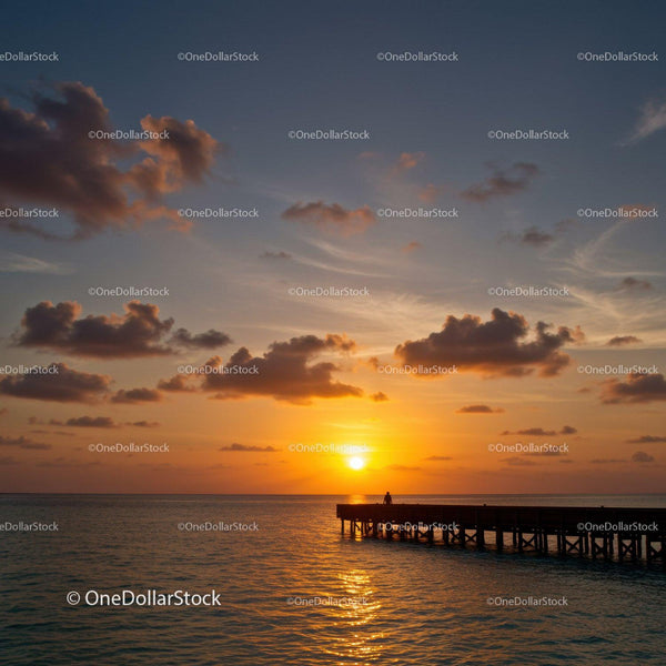 Beautiful Sunset Over Calm Ocean With Pier and Cloudy Sky
