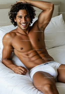 Smiling shirtless man relaxing on bed in white briefs