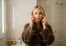 Young Woman Applying Gold Under-Eye Patches in Bathroom