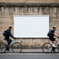 Cyclists passing by blank billboard on stone wall